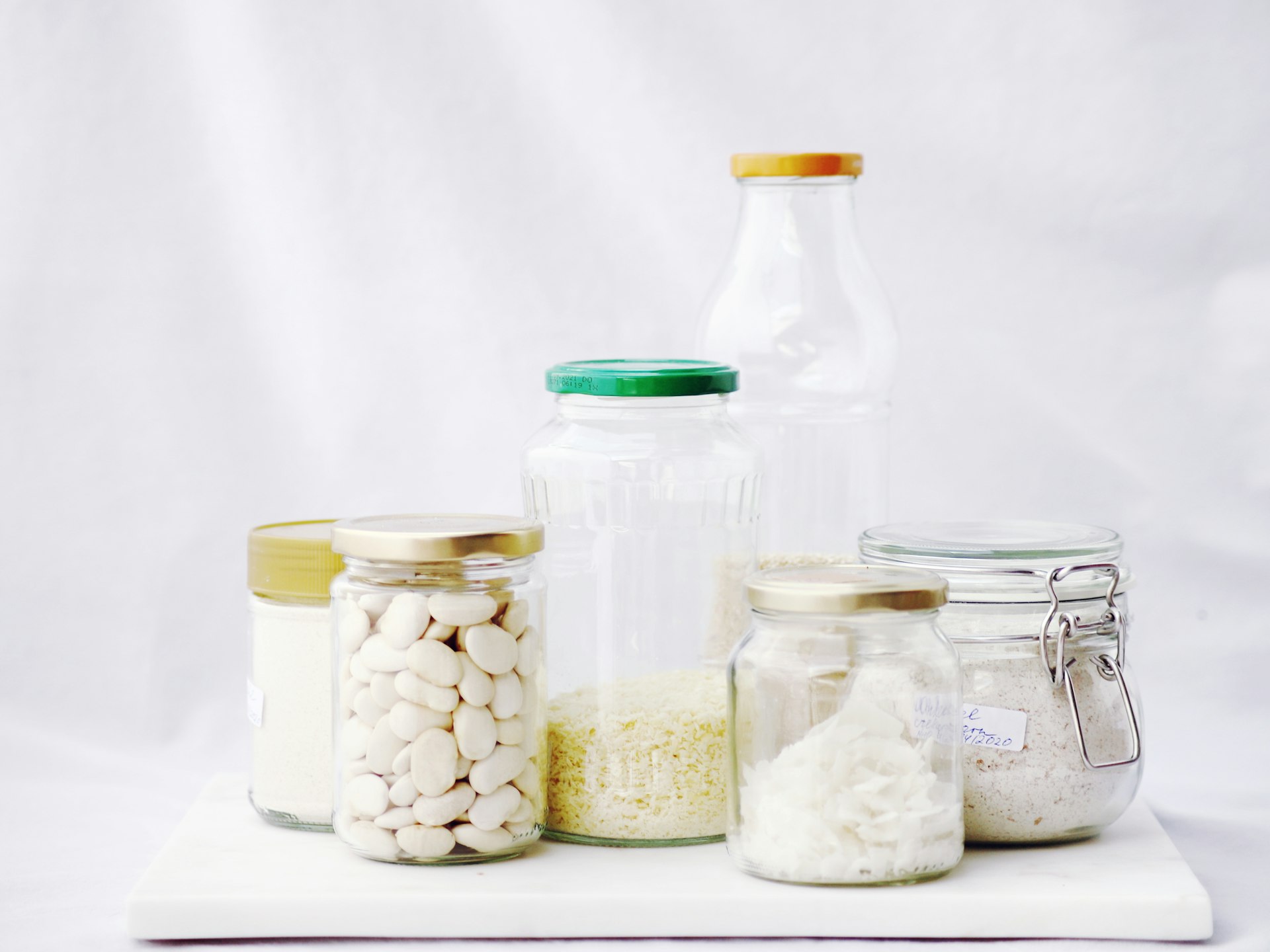 A row of matching clear glass spice jars filled with grains on a clean white pantry shelf